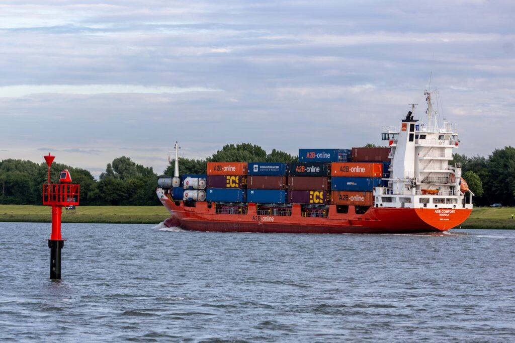 Container ship navigates river waters near buoy at dusk in peaceful setting with clouds